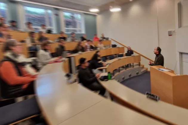 Partially blurred photograph of Markus Lahtinen speaking in front of a lecture hall of people. 