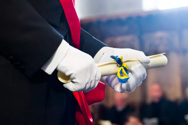 Detail of hands with white gloves holding a rolled-up diploma. Photo