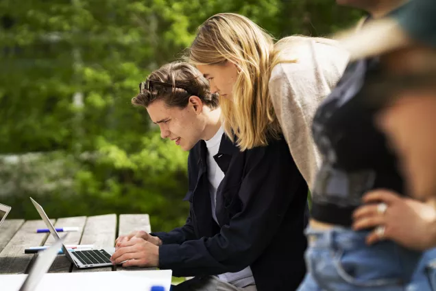 Students outside leaning over a laptop on a table. Photo