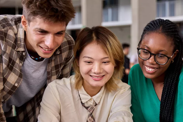 Group of smiling students looking at a laptop screen together. Photo